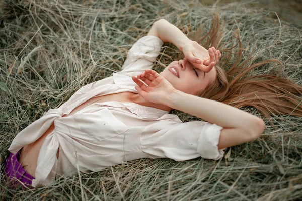 穿着衬衣的年轻微笑的女人躺在干草堆上闭着眼睛 顶部视图 — 图库照片