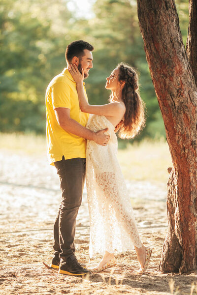 Young enamored couple hugs in forest against background of tree.