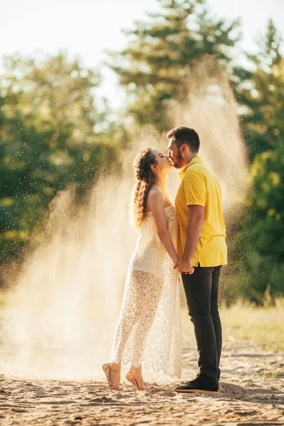 空気で飛んでいる砂の背景に対して森林の愛のキスで若いカップル — ストック写真