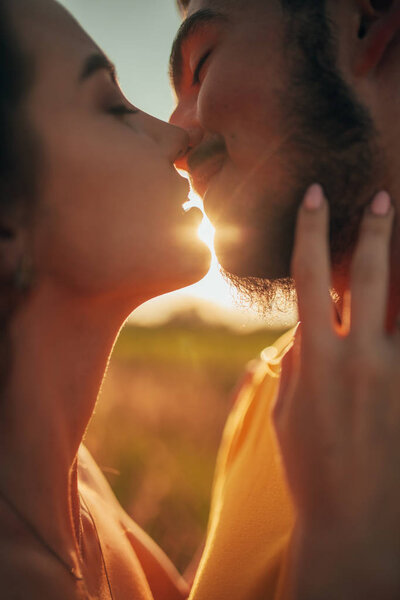 Portrait of kissing enamored couple at meadow. Backlit.