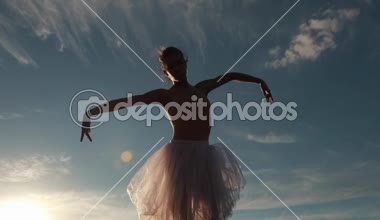 Gün batımında mavi gökyüzü arka plan üzerinde beyaz elbise şeffaf dansları, balerin. Arka ışık. Alt görünümü. 