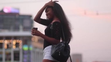 Kahve onun elinde olan kadın anlamına gelir ve akşam saatlerinde caddenin arka plan üzerinde gülümsüyor. Bokeh etkisi.