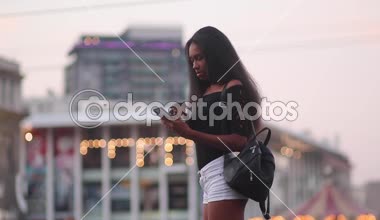 Kahve onun elinde olan kadın duruyor, gülümsüyor, akıllı telefon görüşmeleri ve akşam saatlerinde caddenin arka plan üzerinde onun arkadaşı selamlıyor. Bokeh etkisi.