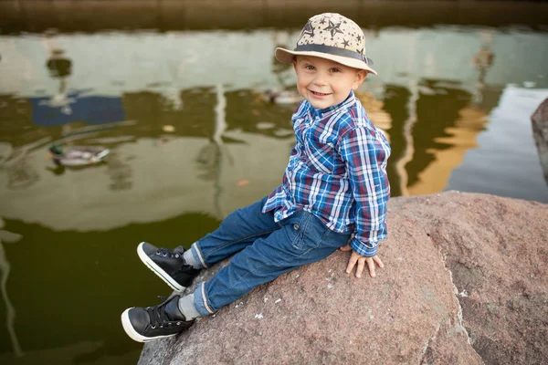 Menino Está Sentado Rocha Durante Passeio Parque Contra Fundo Lago — Fotografia de Stock