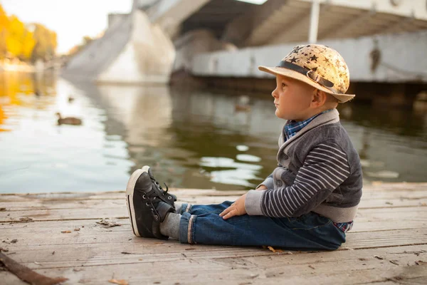 Ein Kleiner Junge Sitzt Neben Dem See Bei Einem Spaziergang — Stockfoto