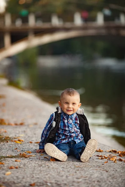 Chlapeček Sedí Vedle Žluté Podzimní Listí Pozadí Jezero Most Během — Stock fotografie