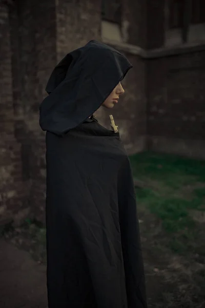 黒カソックとフード付きマントの美しい若い修道女が立っていると祈って彼女の手に渡る 横から見た図 — ストック写真