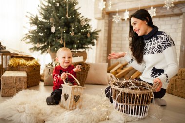 Anne oğluyla halı üzerinde oturan ve Noel ağacı, Festival çelenk ve hediye kutuları karşı artalanda çalışır.