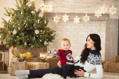 Anne oğluyla halı üzerinde oturan ve Noel ağacı, Festival çelenk ve hediye kutuları karşı artalanda çalışır.