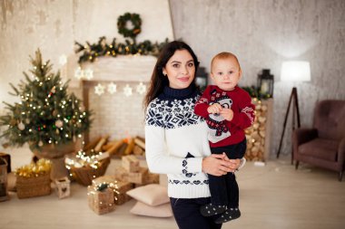 Anne oğluyla Noel ağacı, Festival çelenk, hediye kutuları ve yanan şömine arka plan karşı ayakta.