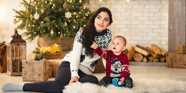 カーペットの上に座っているとクリスマス ツリーとギフト ボックスの背景で遊ぶ息子と母 — ストック写真