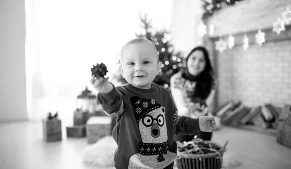 Child boy is playing against the background of the Christmas tree, festive garlands and gift boxes. Black and white image.
