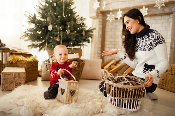カーペットの上に座って クリスマス ツリー お祝い花輪 ギフト ボックスの背景で遊ぶ息子と母 — ストック写真
