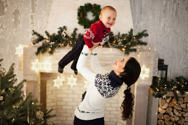 母は彼女の息子と一緒に遊んで クリスマス ツリーとお祝い花輪の背景に彼を投げ — ストック写真