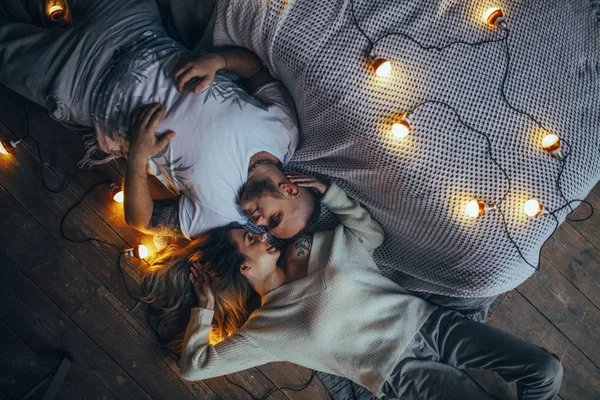 恋爱中的年轻夫妇躺在地板上 微笑着拥抱着发光的灯泡的背景 顶视图 — 图库照片