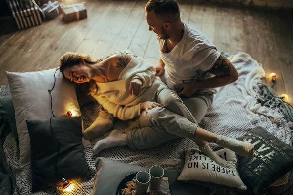 恋爱中的一对夫妇在木地板 枕头和发光的灯泡的背景下快乐地玩耍和大笑 — 图库照片