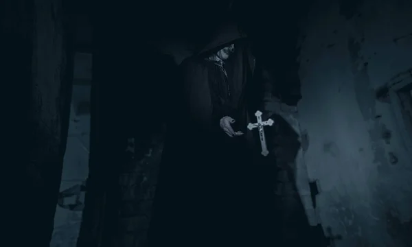 黒いフード付きマントを着た女性は 悪魔に憑かれた尼僧のイメージで空を飛んでクロスの横にある闇の中に立っています コスプレ — ストック写真