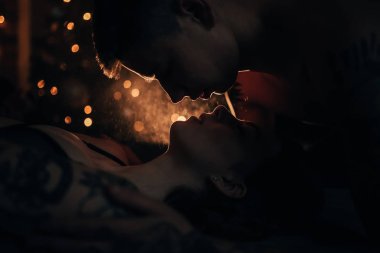 Yüz yüze ve öpüşme aydınlatmalı lamba ışığında karşı yalan aşık genç çift portresi. Bokeh etkisi ile.