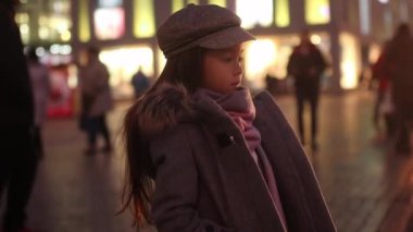 Çocuk bir ceket, şapka ve atkı ayakta ve bekleyen insanlar tarafından geçen ve şehir ışıkları akşam arka plan karşı Street kızıdır