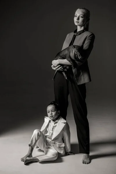 Young mother with black vietnamese piglet on her hands is posing in studio with her little daughter. Black and white image. Concept of the Chinese New Year of the Pig.