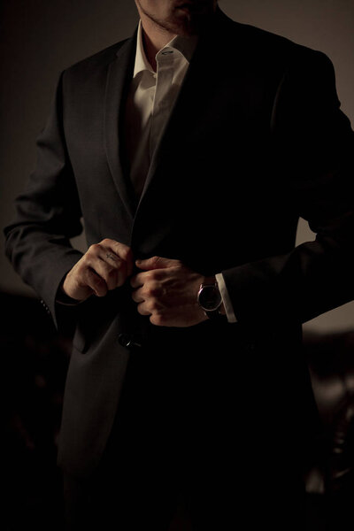 Молодой бизнесмен в черном костюме и белой рубашке стоит и застегивает куртку.
.