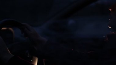 Genç bir kadın geceleri araba direksiyon başında oturuyor. Arabayı yan pencereden görüntüleme.