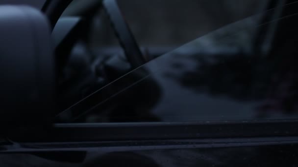 Une jeune femme est assise au volant d'une voiture le soir. Vue par la fenêtre latérale de la voiture .