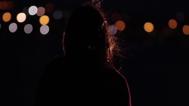 思慮深い女性は夜の街の明かりの背景に風の夜立っています — ストック動画