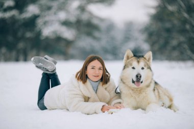 Kız yanında bir köpek Alaskan Malamute karda yalan söylüyor ve onun kışın yürüyüşe sarılarak.