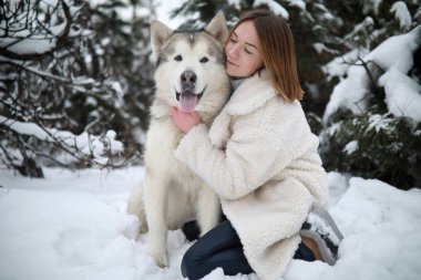 Kızlar Kış Forest pines arka plan karşı yürüyüşe köpek Alaskan Malamute sarılma.