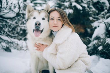 Kızlar Kış Forest pines arka plan karşı yürüyüşe köpek Alaskan Malamute sarılma.
