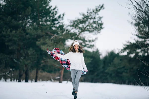 年轻女子在冬天的松林里跑着微笑着 手里拿着围巾 — 图库照片