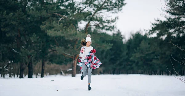 年轻女子在冬天的松林里跑着微笑着 手里拿着围巾 — 图库照片