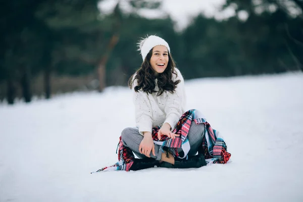 在冬天的散步中 美丽的女人坐在雪地上笑着 穿着白色毛衣 帽子和围巾 — 图库照片