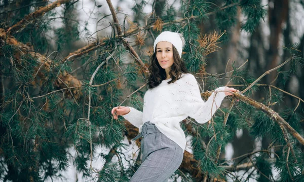 冬の森で散歩中に倒れた松の木のトランクの横に若い女性が立っています — ストック写真