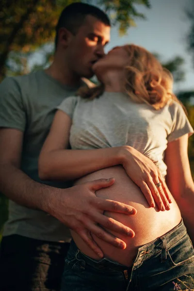 Bir adam onun hamile eşi göbek kucaklayan ve yürüyüş sırasında onu öper. Portre.