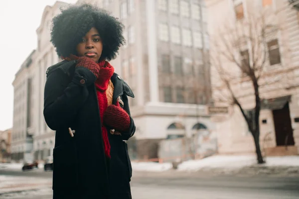 Young black woman is standing at city street against background of buildings.