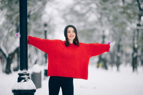穿着红色毛衣的微笑的女孩在冬天的雪街上有乐趣 — 图库照片