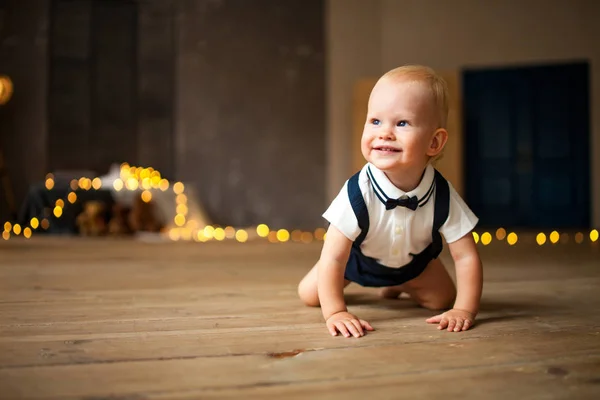 Smiling baby boy crawls at the floor against background of garland of glowing light bulbs. Copy space.