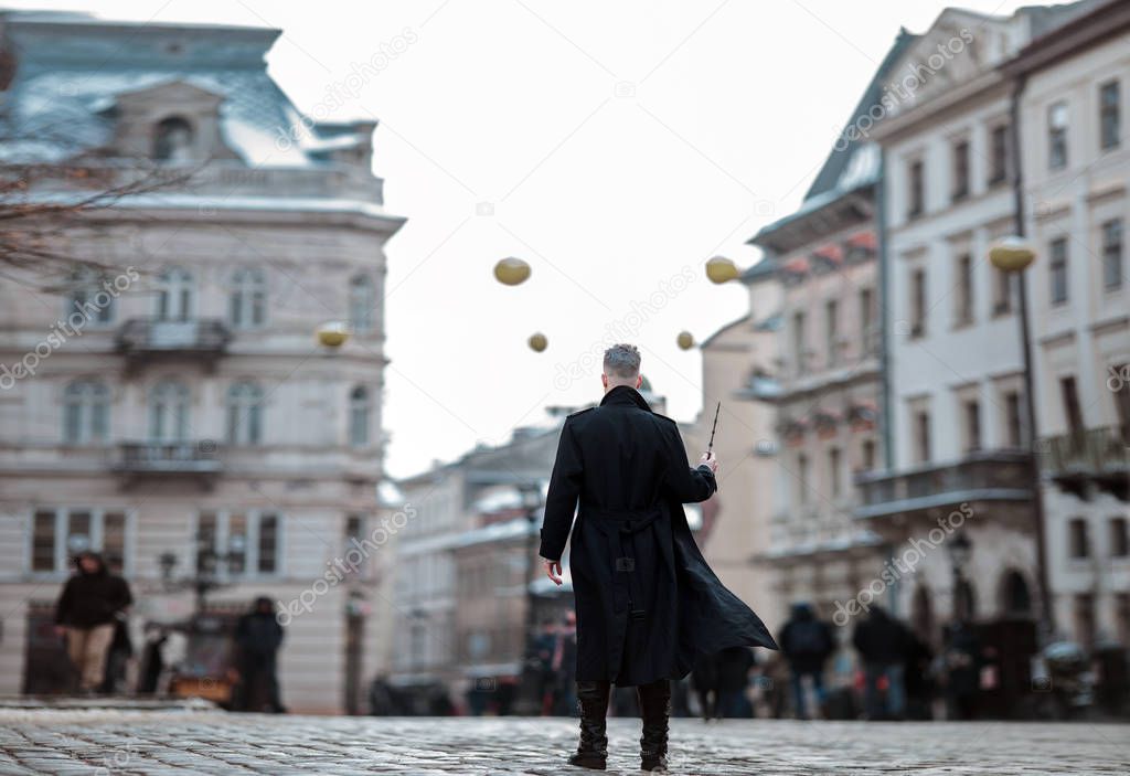 Young man in image of black magician walks on city street with magic wand in his hand.