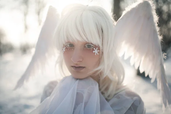 Portrait of beautiful blonde girl in image of good angel with wings dressed in white clothing.