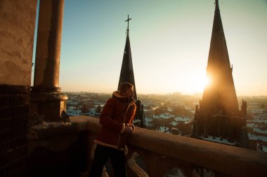 Genç biri Balkonda duran ve kilise kule çerçevede cityscape, günbatımında bakar.