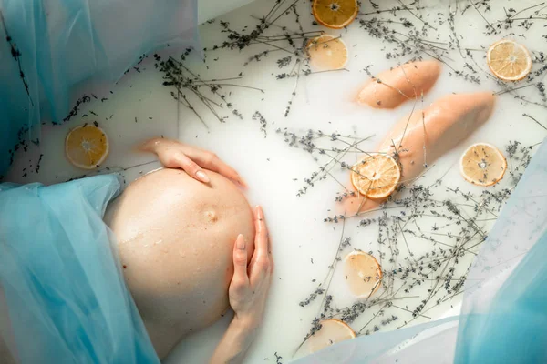 Terhes nő vesz egy fürdőt, tej, levendula fűszernövények és narancs — Stock Fotó