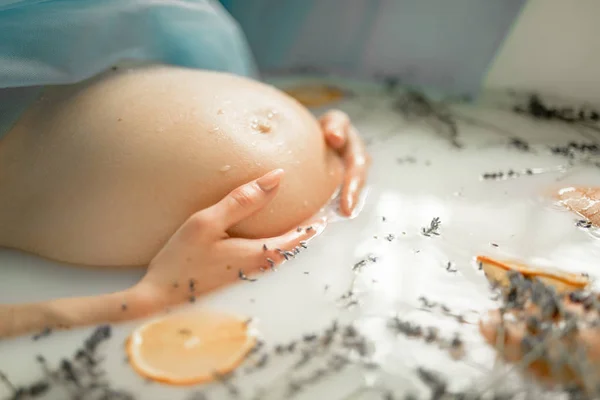Terhes nő vesz egy fürdőt, tej, levendula fűszernövények és narancs — Stock Fotó
