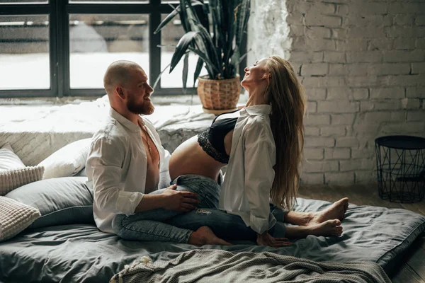 Pregnant woman has a fun with her husband on a bed. — Stock Photo, Image