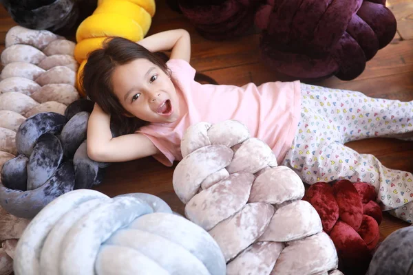 Niña juega en el suelo entre almohadas inusuales en pijama . — Foto de Stock