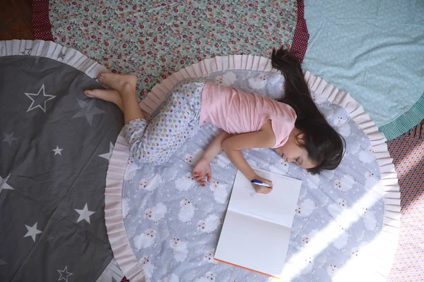子供の女の子がマットに横たわって、アルバムに描く. — ストック写真