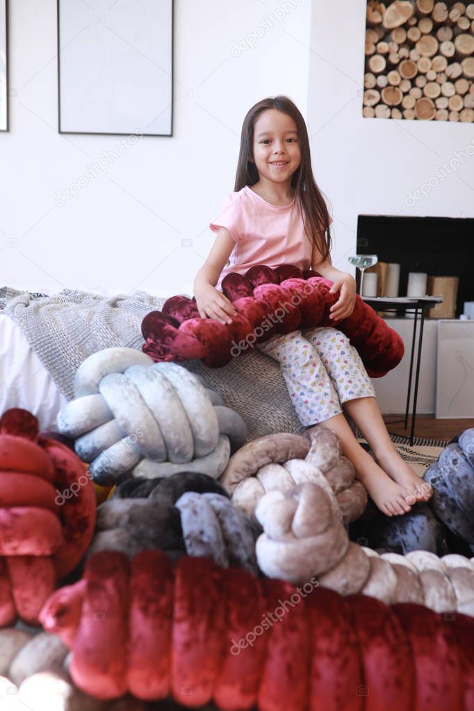 Child girl plays among unusual pillows in pajamas.