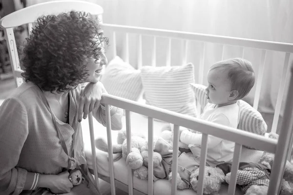 Feliz madre se sienta junto a su bebé en la cuna . — Foto de Stock