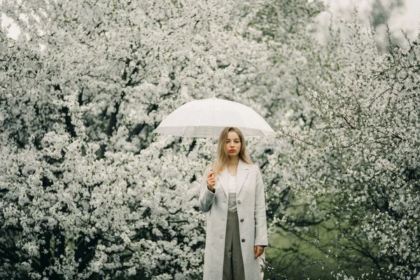 En kvinna slappnar av med paraply i händerna bland blommande träd — Stockfoto